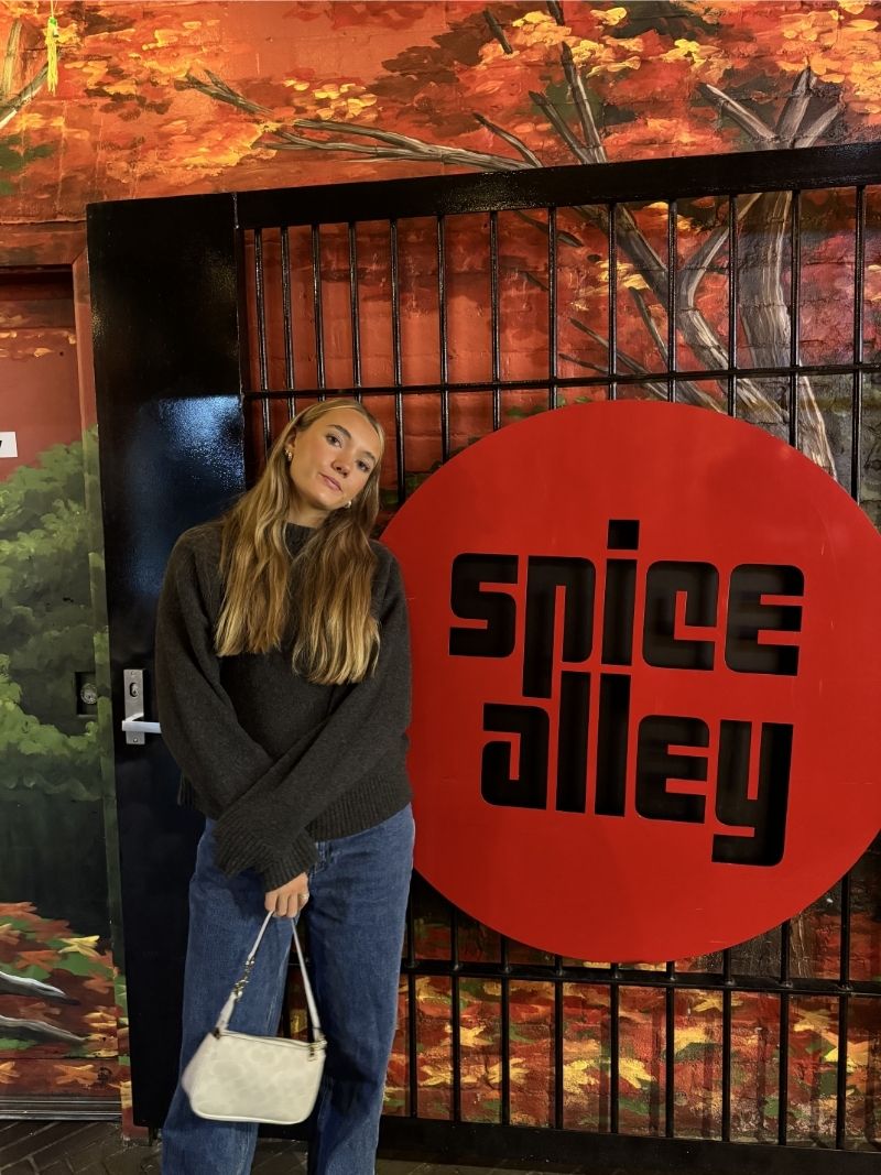 Asha Thomson standing in front of the Spice Alley sign in Chippendale, red circle logo and painted mural behind her, during a family trip in April